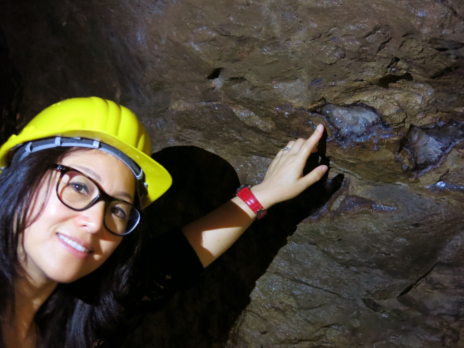 Kehan Li in a yellow hard hat inside a jadeite mine on the Yunnan–Myanmar border, hand resting against the rough rock face.